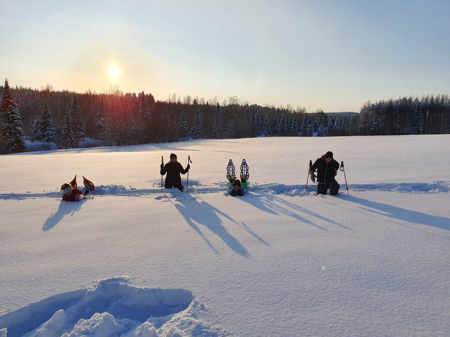 Neljä nuorta poseeraa lumikengissä peltoaukiolla.